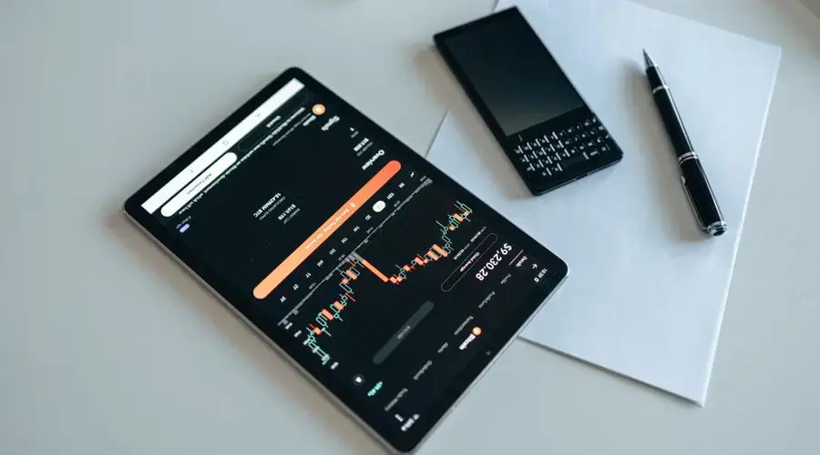 Close-up of finance app on tablet with phone and pen on white table.