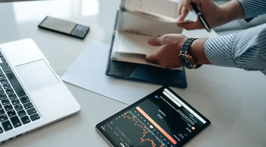 Professional workspace featuring a laptop, tablet with analytics, and a person organizing documents.