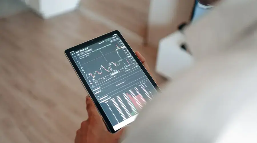 Close-up of person using a tablet displaying trading graphs indoors.