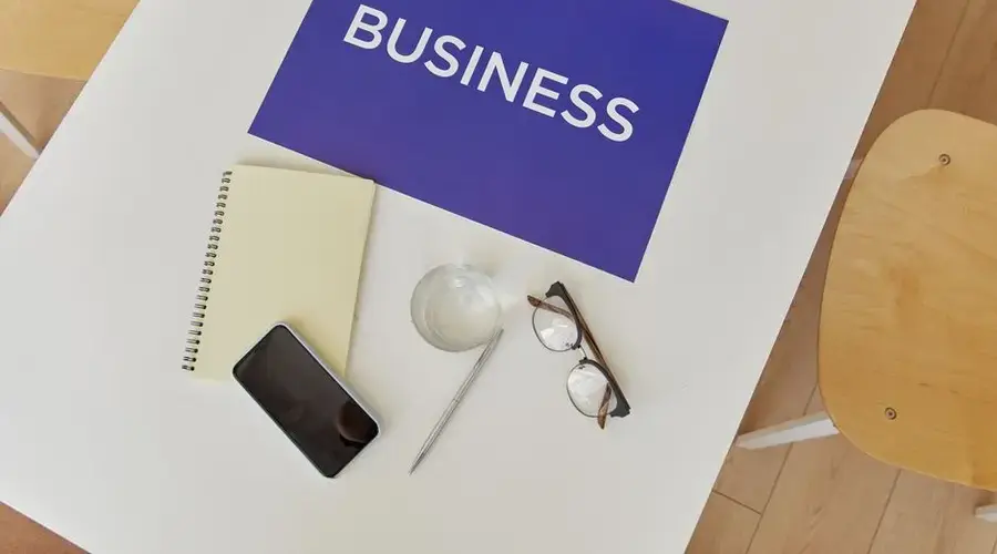 Top view of a minimalist business workspace with essentials like notebook, phone, glasses, and a business sign.