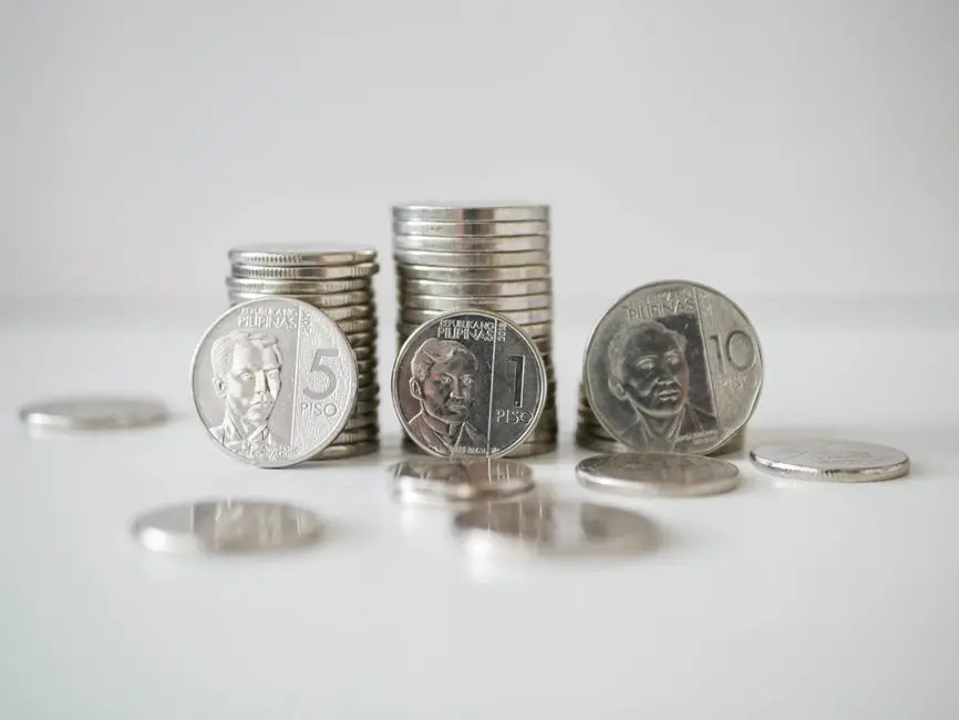 Stacked and scattered Philippine Peso coins in a close-up view on a white surface.