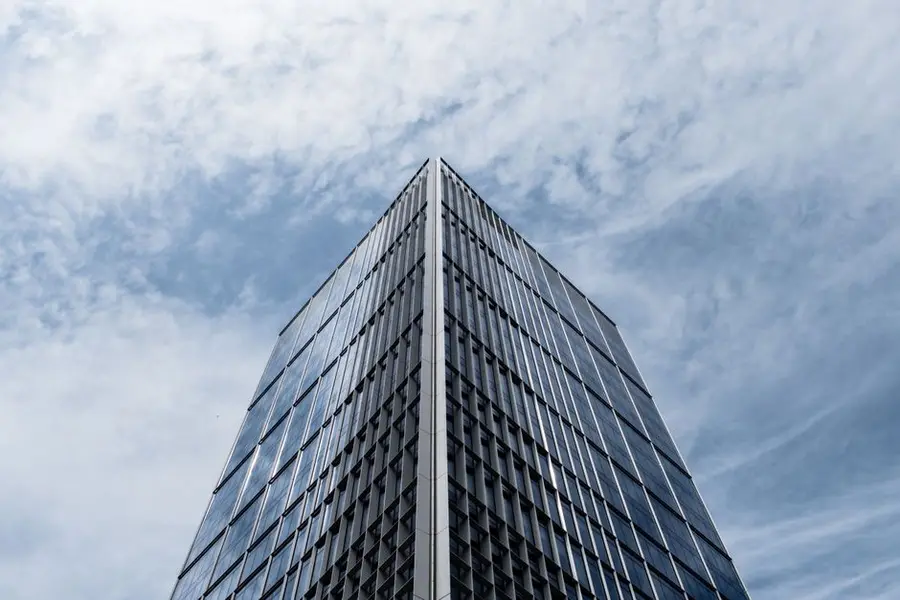 Low angle view of a modern glass skyscraper with a cloudy sky backdrop.