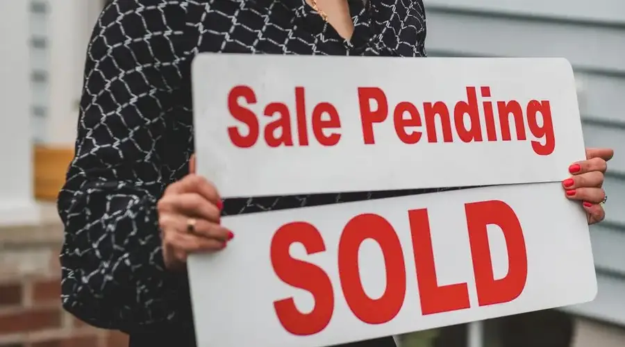A businesswoman holding 'Sale Pending' and 'Sold' signs indicating a successful real estate transaction.