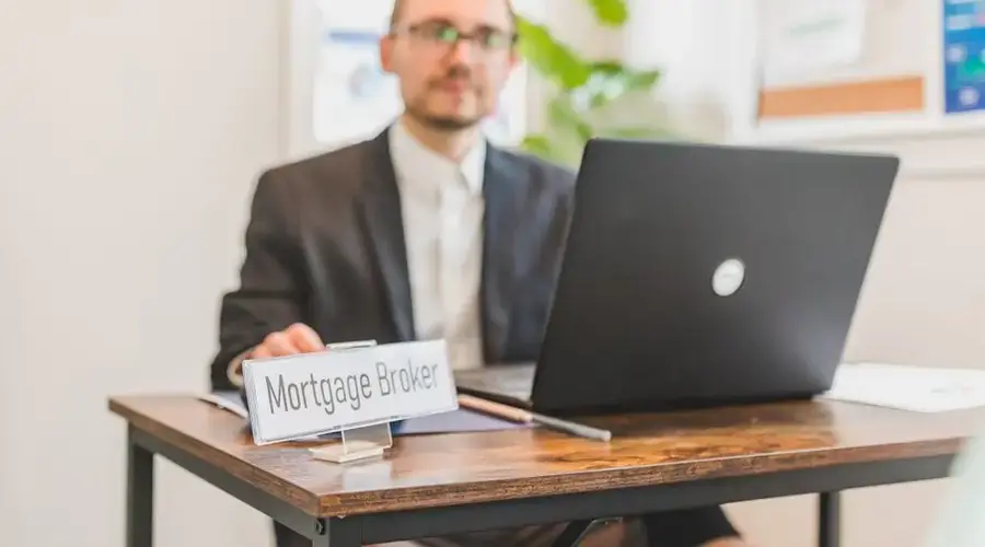 A mortgage broker working at a desk with a laptop in an office setting.