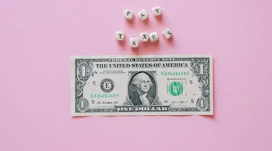 US one dollar bill on a pink background with pay taxes reminder cubes.