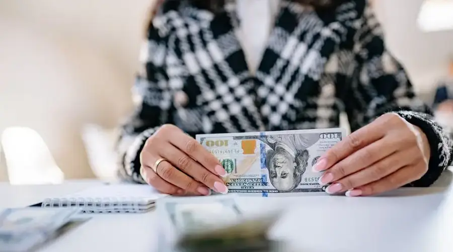 Close-up image of hands holding a US hundred dollar bill on a desk.