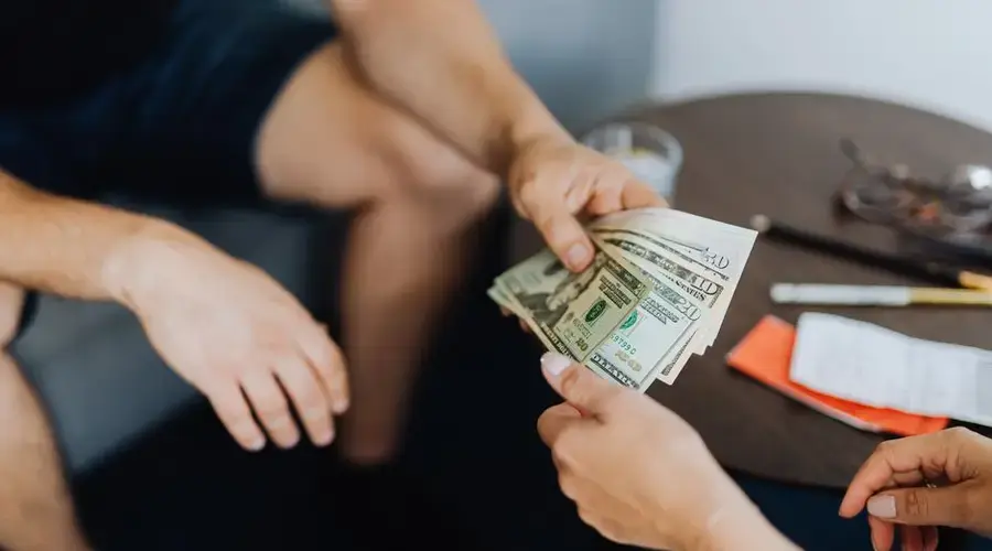 Close-up of hands exchanging US dollar bills, symbolizing a financial transaction or payment.