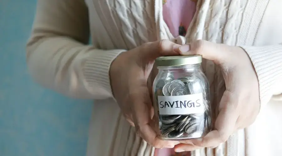 Woman holding a jar labeled 'savings' filled with coins, representing financial savings.