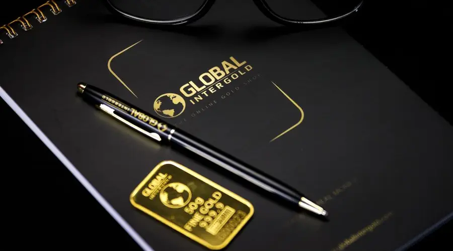 An elegant setup with a notebook, pen, and gold bar, embodying luxury and style.