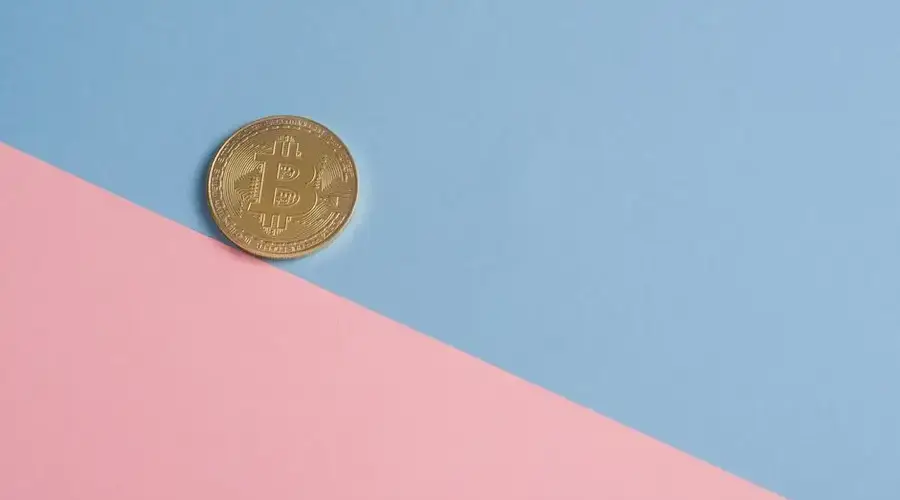 A single gold Bitcoin on a minimal pastel blue and pink background.