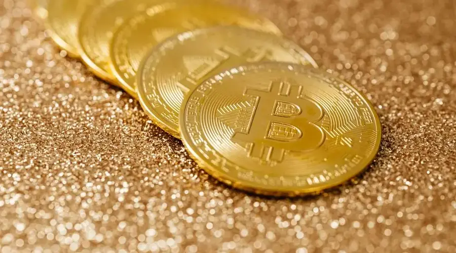 Shiny gold bitcoin coins placed on a textured glitter surface, highlighting cryptocurrency.