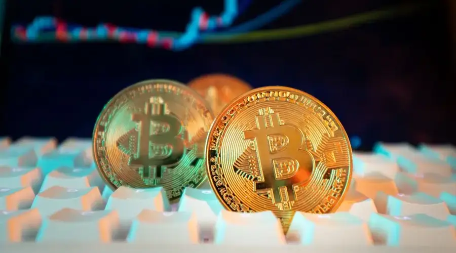 Golden Bitcoin coins on a keyboard with a financial chart in the background, representing digital currency and market trends.