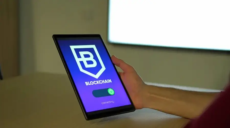 A hand holding a tablet with blockchain logo on screen, showcasing digital technology.