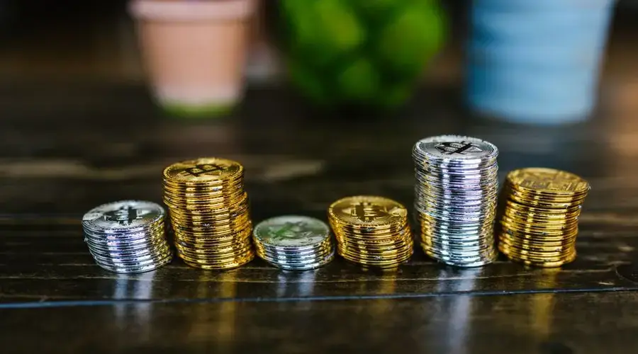 Pile of shiny gold and silver cryptocurrency coins on a wooden table.