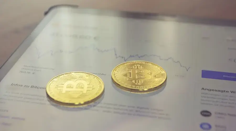 Close-up of two golden Bitcoin coins on a tablet screen displaying financial data.