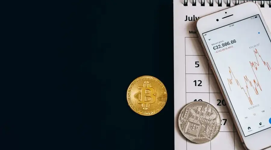 Bitcoin coins on a calendar with a smartphone showing price trends, illustrating finance dynamics.