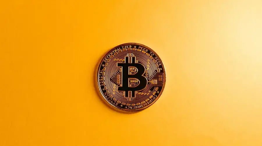 A close-up of a Bitcoin coin on a bright yellow background, symbolizing digital currency.
