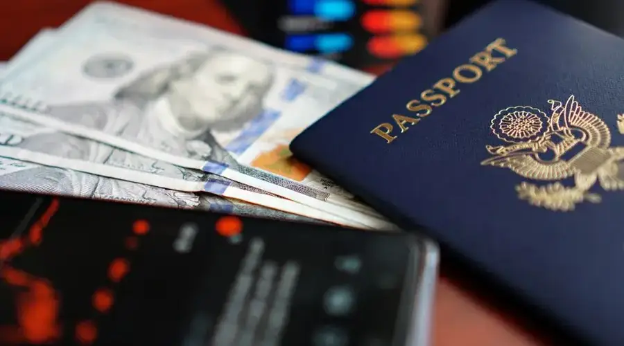 A close-up image of a U.S. passport, dollar bills, and a smartphone.
