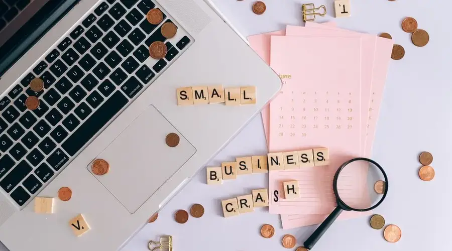 Flatlay of a laptop, coins, and scrabble tiles spelling 'small business crash'.