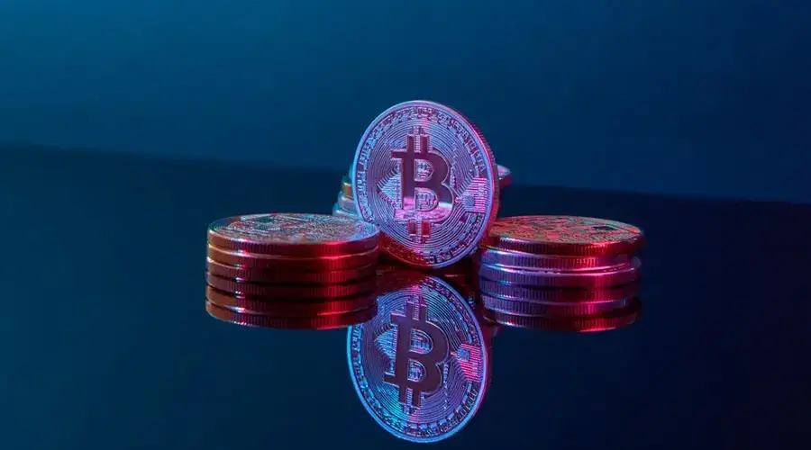 Stacked bitcoin coins on a reflective surface with a vibrant digital glow, symbolizing wealth and cryptocurrency.