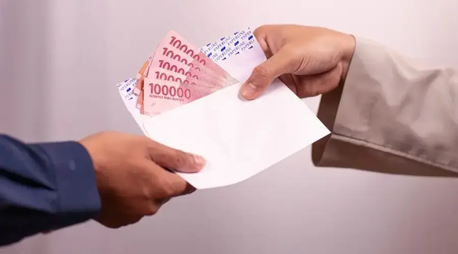 Hands giving and receiving Indonesian rupiah in an envelope, symbolizing financial transaction.