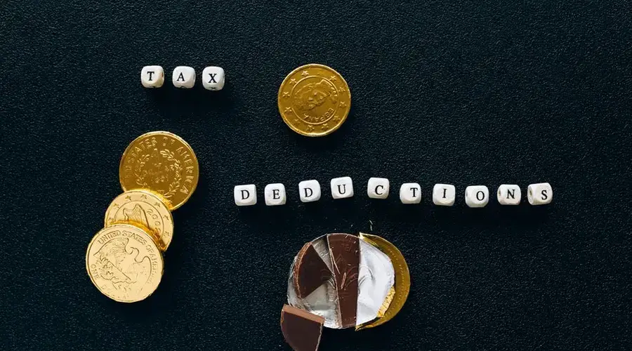 Creative concept of tax deductions using chocolate coins and letter tiles on a black background.