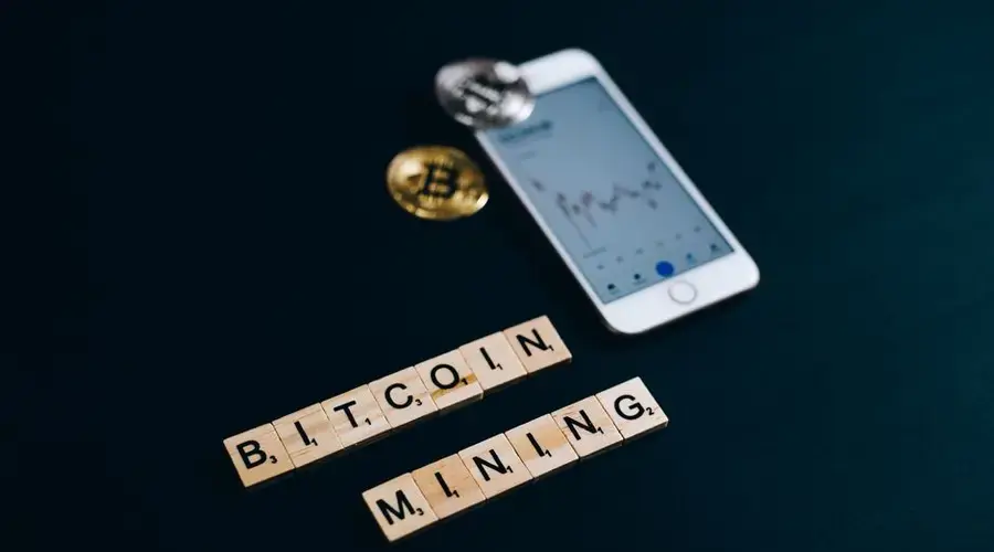 A visual representation of bitcoin mining with smartphone and blockchain concept using Scrabble pieces.