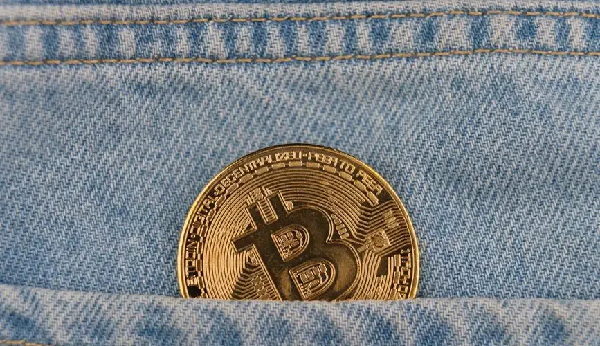 Close-up of a bitcoin coin in a denim pocket, symbolizing cryptocurrency and finance.