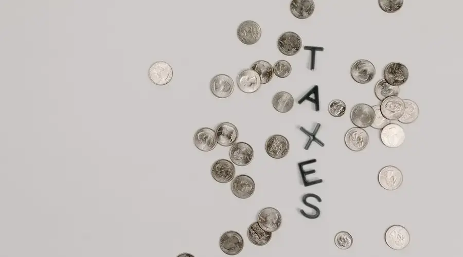 Scattered coins forming the word 'TAXES' on a white surface, symbolizing financial concepts.