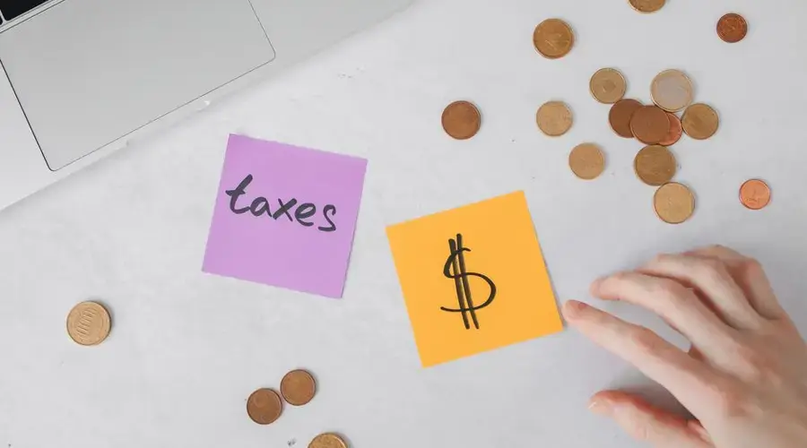 Overhead view of coins, sticky notes with tax symbols, and a hand on a desk.