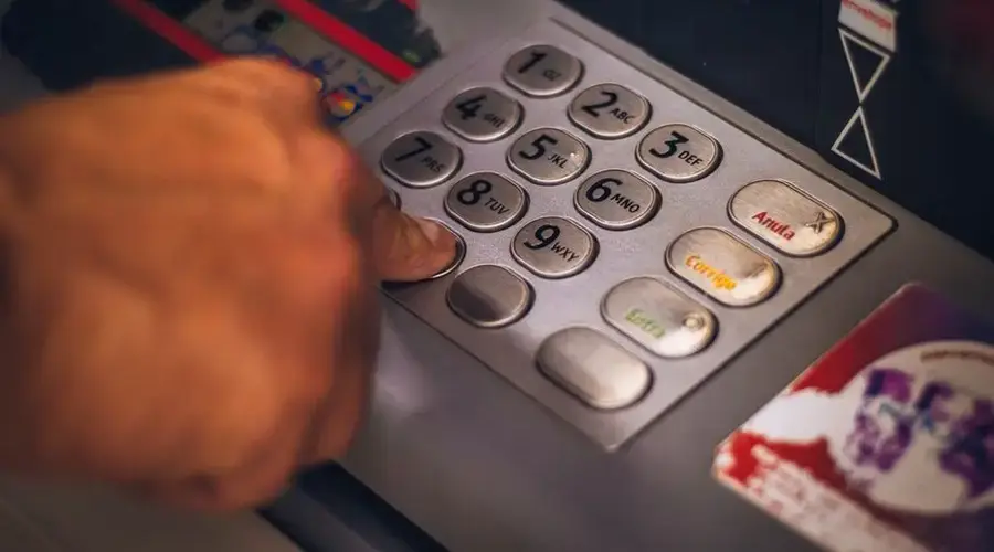 A hand pressing a button on an ATM keypad in Brasil, emphasizing digital banking.