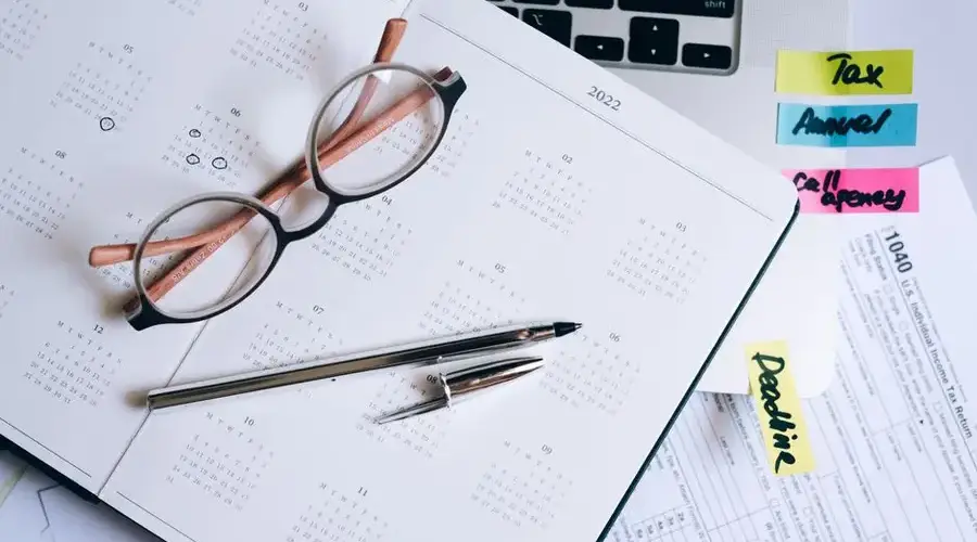 Overhead view of a desk with glasses, a pen, calendar, and tax documents.