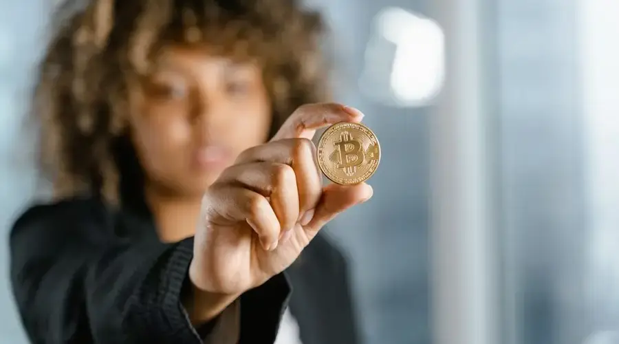 Focused young woman holding a Bitcoin coin indoors close-up, symbolizing cryptocurrency.