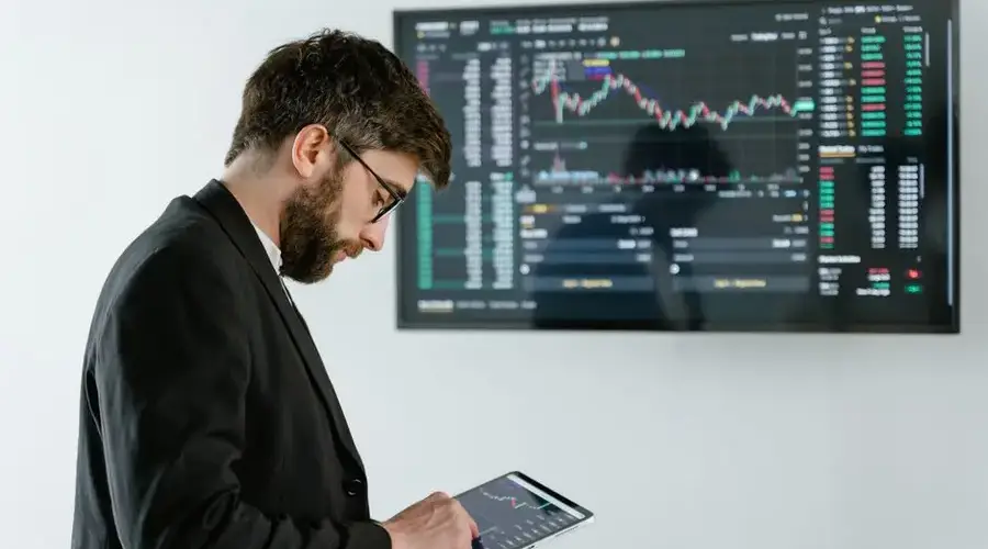 Professional man using tablet in front of cryptocurrency trading screen indoors.
