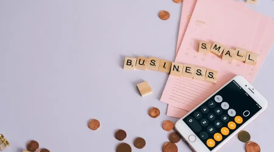 Flat lay of a small business planning scene with coins, smartphone calculator, and letter tiles.