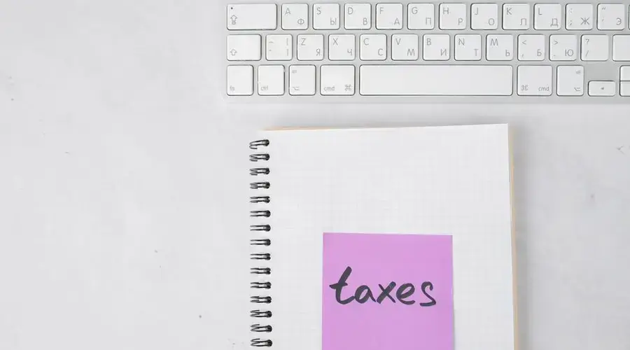 Top view of a notebook with a 'taxes' sticky note beside a keyboard, ideal for finance themes.