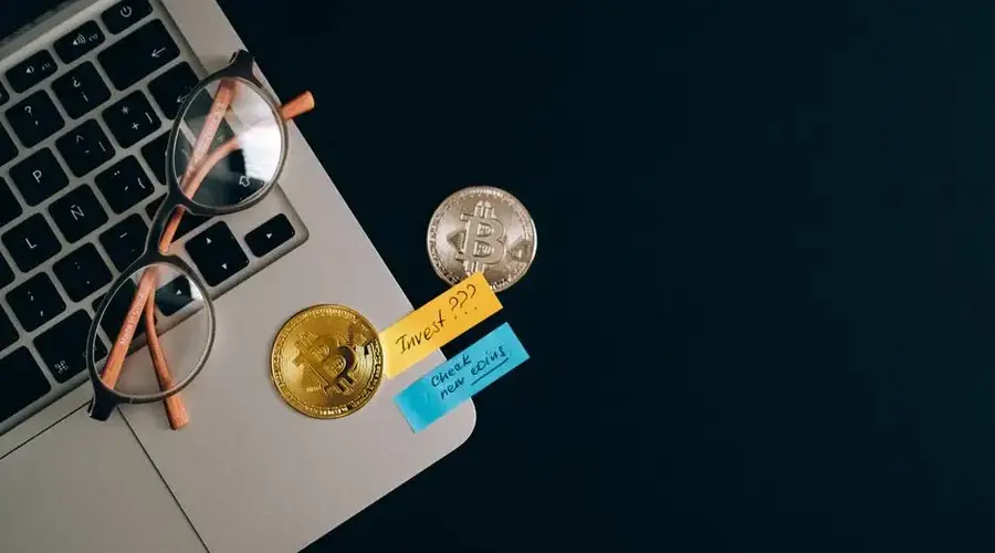 Laptop, bitcoins, and notes on a desk representing cryptocurrency investment concept.