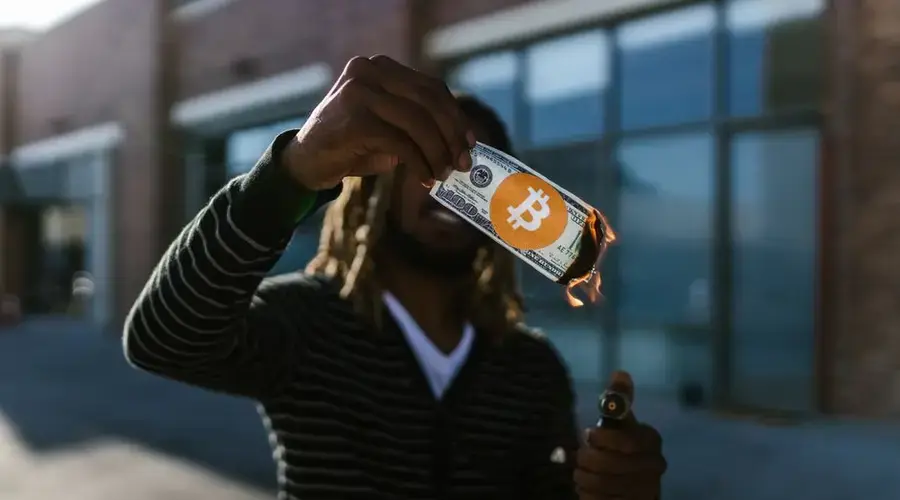 Man holding a burning dollar bill with Bitcoin symbol. Conceptual image of cryptocurrency impact.