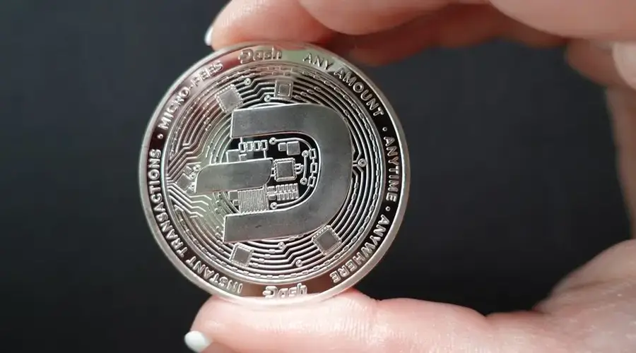 A close-up image showcasing a Dash coin held between fingers, emphasizing cryptocurrency and digital finance.