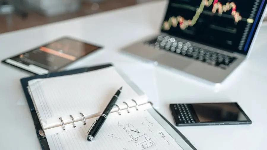 Open notepad on desk with pen, laptop, and tablet, suggesting office work setting.