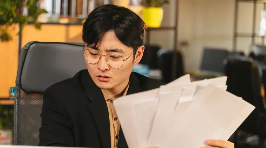 Businessman in glasses reviewing paperwork in a modern office setting.