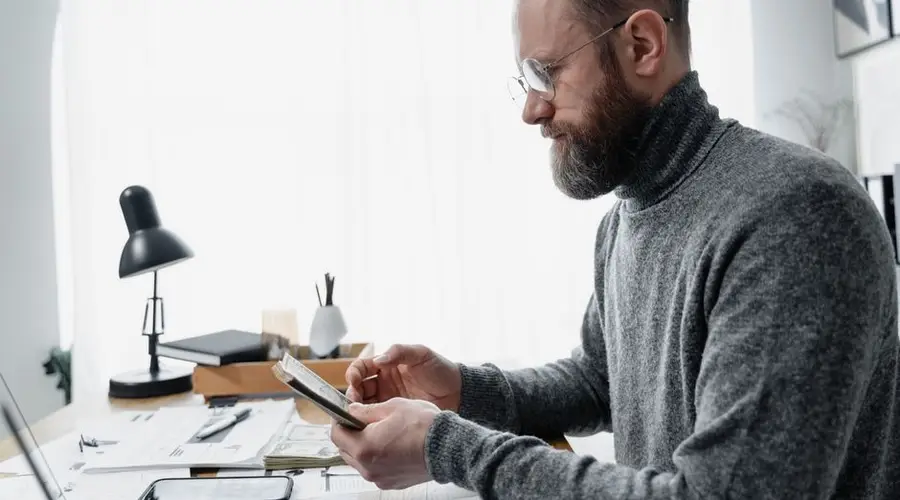 Adult male reviewing documents at a desk with a modern setup, conveying focus and concentration.