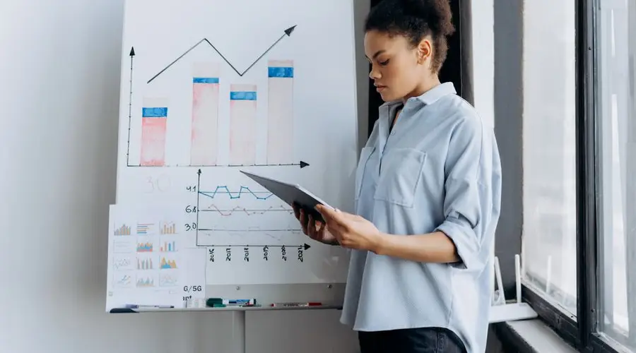 A woman analyzing sales data on a tablet next to a presentation board with graphs.