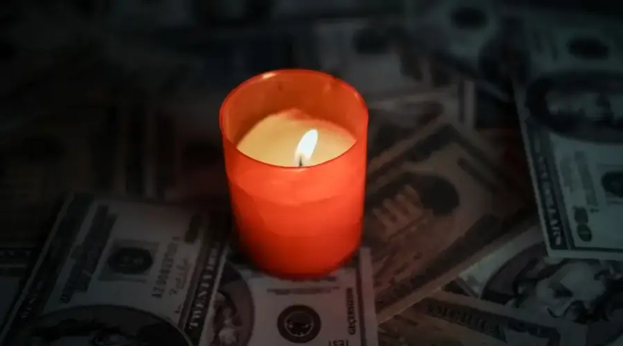 A red candle glowing among scattered US dollar banknotes, creating a dramatic ambiance.