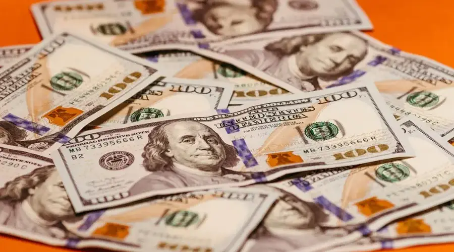Scattered US $100 bills on a vibrant orange surface symbolizing wealth and finance.