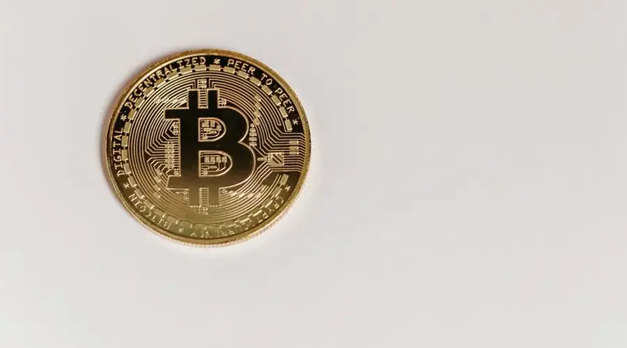 High-quality close-up of a gold Bitcoin coin on a white surface, emphasizing digital currency.