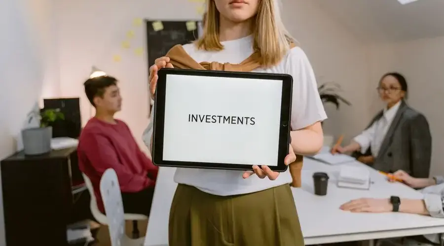 Young professional holding tablet in team meeting focused on investments.