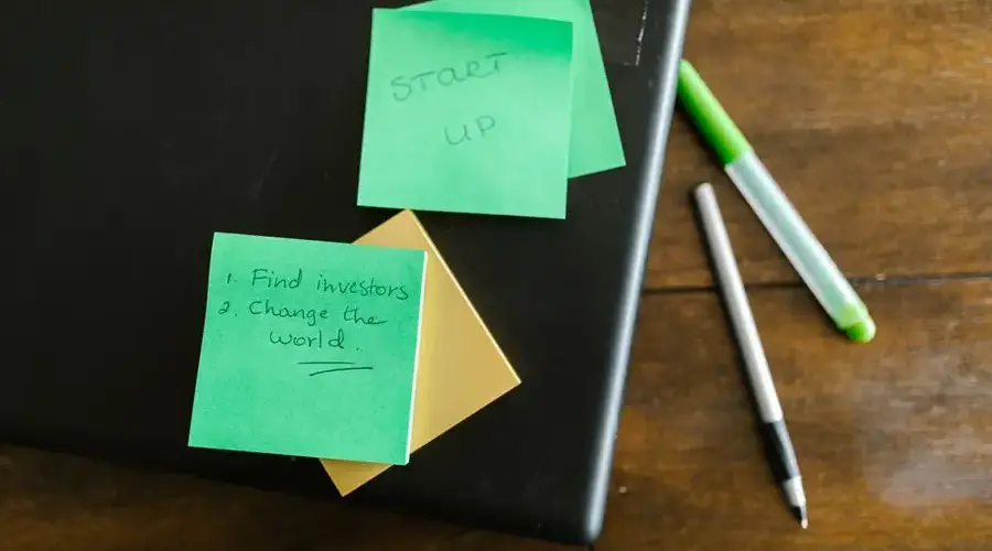 Green sticky notes with startup goals on a wooden desk with pens.