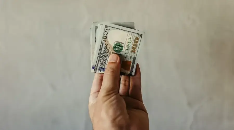 A clear view of a human hand holding a stack of US dollar bills, symbolizing finances.