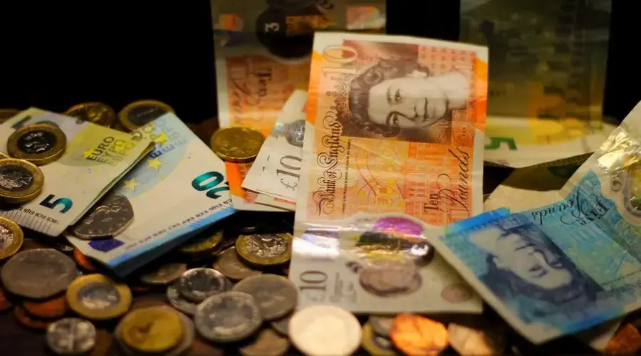 A dark-toned close-up of various Euro and Pound banknotes and coins scattered.